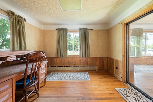 home office featuring light wood-style floors, a textured ceiling, baseboard heating, and a wainscoted wall