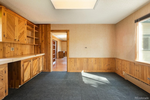 empty room featuring a textured ceiling, wainscoting, a baseboard radiator, and dark carpet