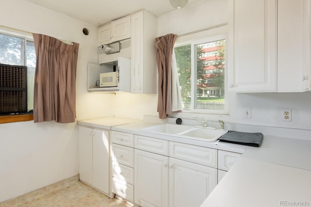 kitchen with a healthy amount of sunlight, white microwave, white cabinets, and a sink