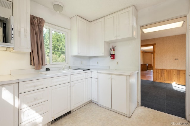 kitchen with a wainscoted wall, wooden walls, white cabinets, and a sink