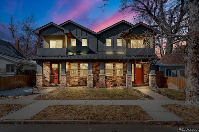 view of front of home featuring board and batten siding, a standing seam roof, fence, and stone siding