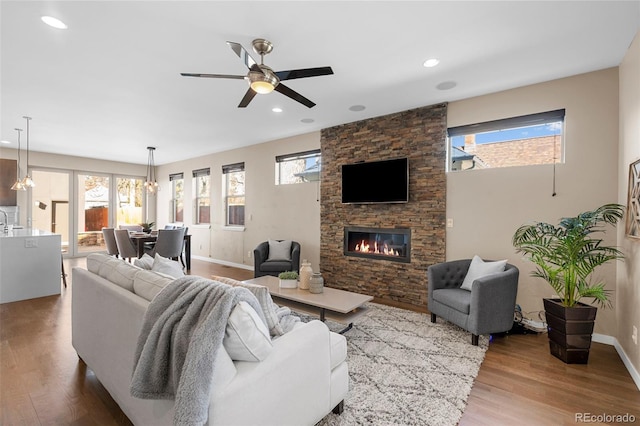 living area with baseboards, a ceiling fan, wood finished floors, and a stone fireplace