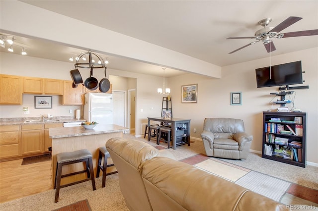 carpeted living room featuring ceiling fan with notable chandelier, sink, and beam ceiling