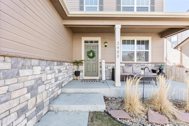 property entrance featuring covered porch, stone siding, and fence