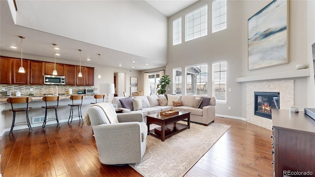 living room with a tile fireplace, a towering ceiling, and dark wood-type flooring