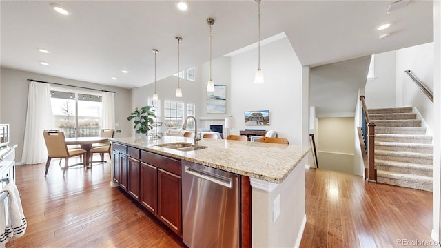 kitchen featuring a center island with sink, sink, stainless steel dishwasher, light stone countertops, and decorative light fixtures