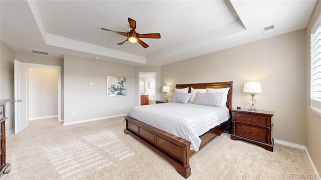 bedroom with ceiling fan, light carpet, and a tray ceiling