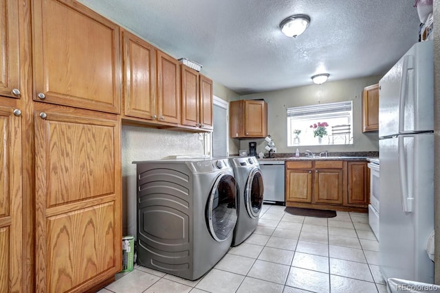 laundry room featuring sink, light tile patterned floors, a textured ceiling, and washing machine and clothes dryer