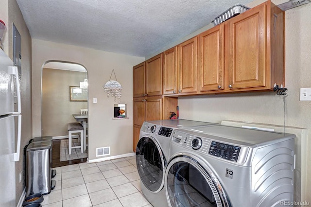 clothes washing area with independent washer and dryer, cabinets, light tile patterned floors, and a textured ceiling