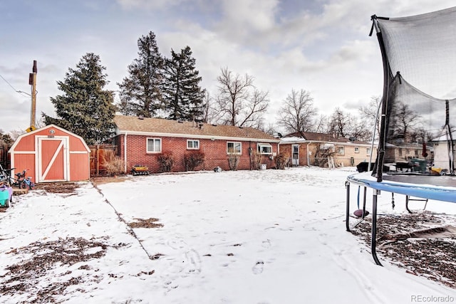 yard covered in snow featuring a storage unit and a trampoline