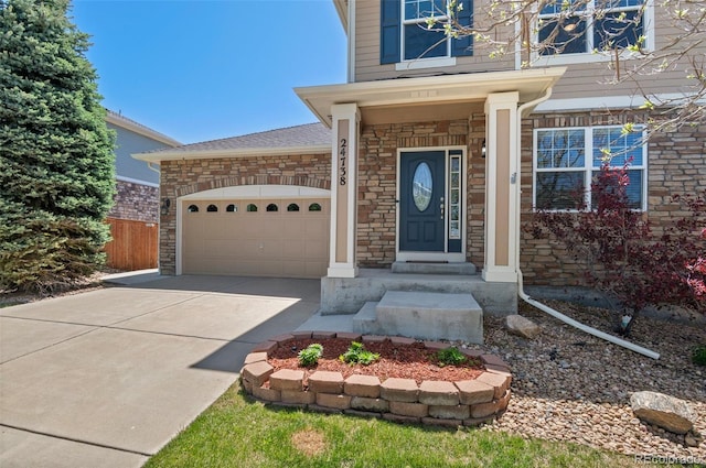 24738 E Layton Pl, Aurora, CO 80016 - view of exterior entry with driveway, stone siding, a garage, and fence
