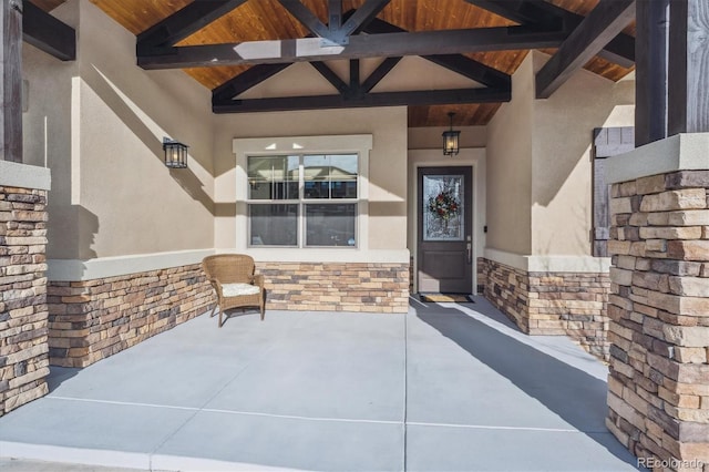 entrance to property with a patio, stone siding, and stucco siding