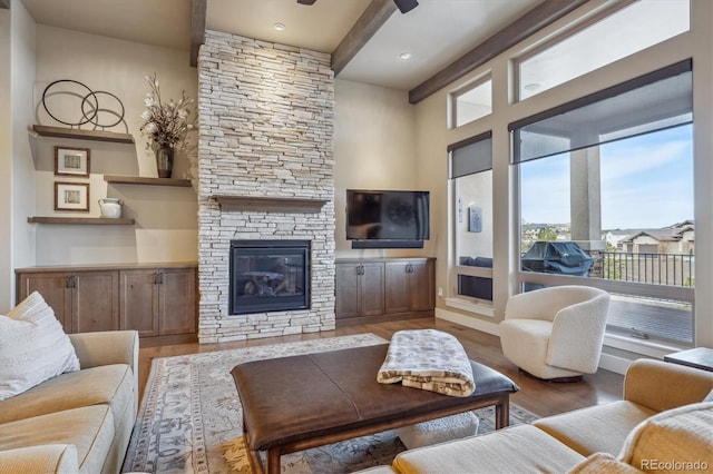 living room featuring a stone fireplace, beam ceiling, and wood finished floors