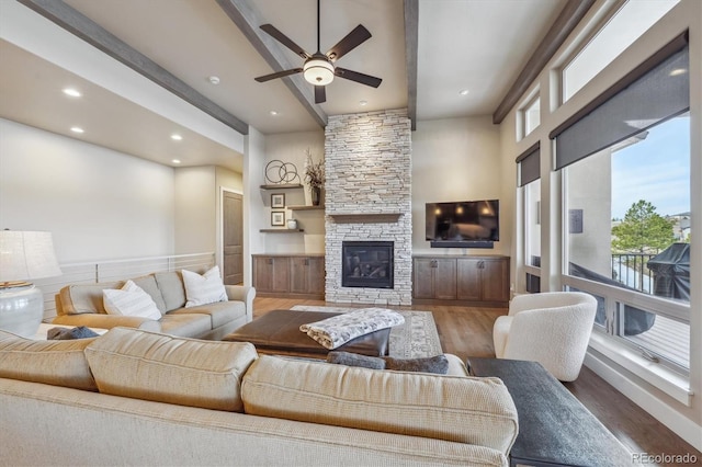 living room featuring ceiling fan, beamed ceiling, a stone fireplace, recessed lighting, and wood finished floors