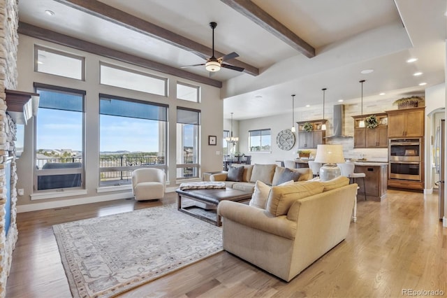 living area featuring beamed ceiling, ceiling fan with notable chandelier, recessed lighting, light wood finished floors, and baseboards