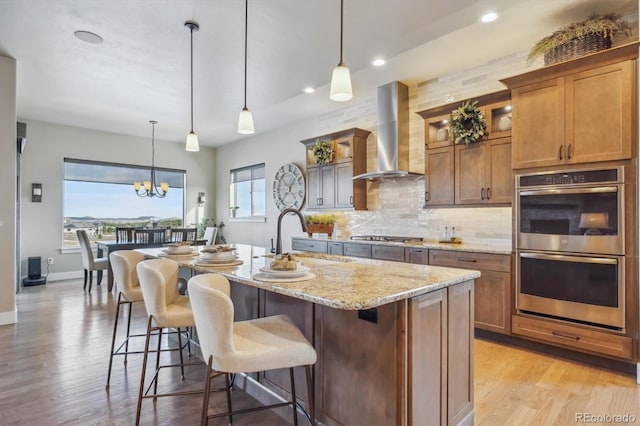 kitchen with backsplash, light stone countertops, appliances with stainless steel finishes, wall chimney exhaust hood, and a sink