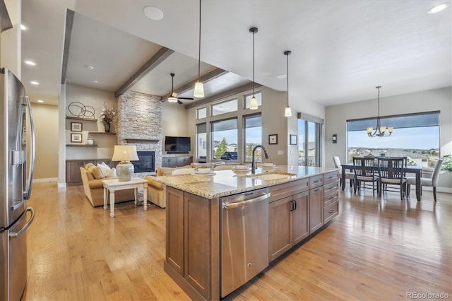 kitchen with light wood-type flooring, a sink, appliances with stainless steel finishes, a stone fireplace, and light stone countertops