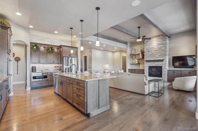 kitchen with decorative light fixtures, appliances with stainless steel finishes, a fireplace, light wood-style floors, and a sink