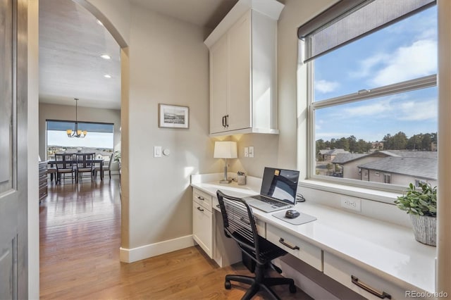 office area with built in desk, arched walkways, an inviting chandelier, light wood finished floors, and baseboards