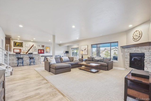 living room with a stone fireplace, recessed lighting, a bar, and wood finished floors