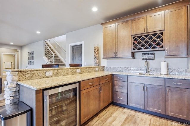 kitchen with light stone counters, beverage cooler, a peninsula, light wood-style flooring, and a sink