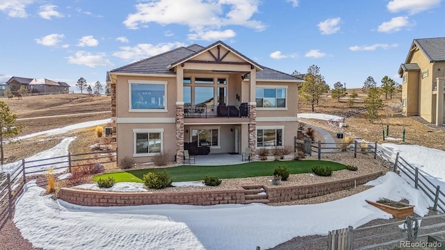 snow covered rear of property with stucco siding, a fenced backyard, a yard, a balcony, and a patio area