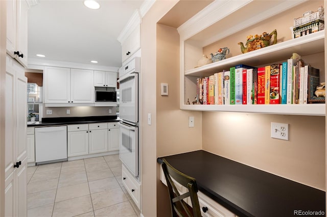 kitchen featuring white appliances, light tile patterned floors, white cabinets, built in study area, and dark countertops