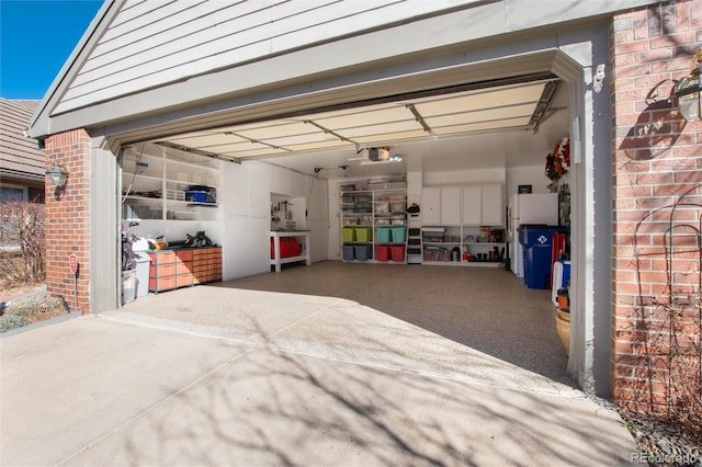 garage featuring a garage door opener, freestanding refrigerator, and driveway