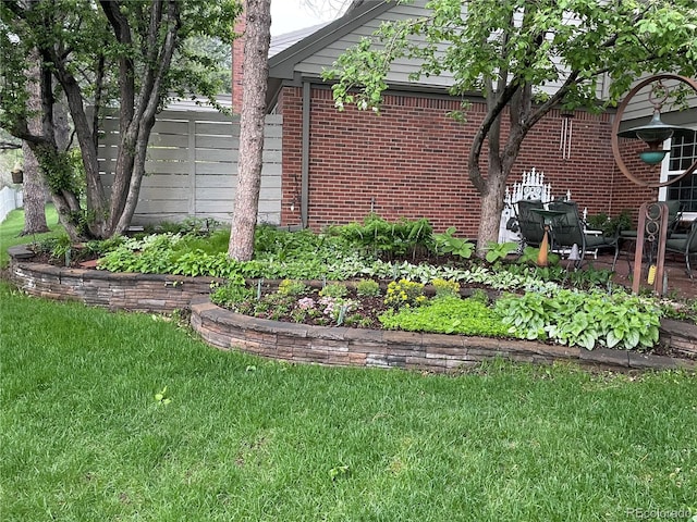 view of side of property with brick siding, a lawn, and fence