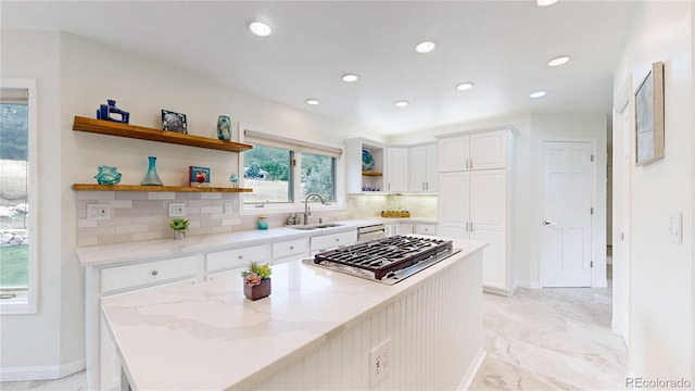 kitchen featuring white cabinets, light stone countertops, stainless steel gas stovetop, open shelves, and a sink