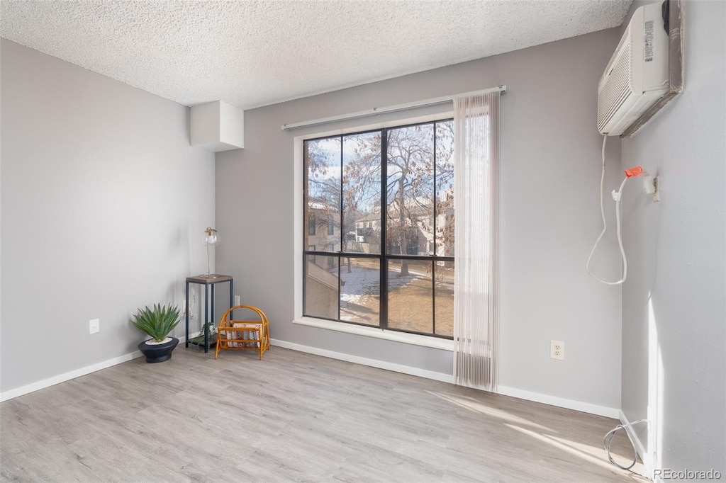 unfurnished room featuring a wall mounted air conditioner, light hardwood / wood-style floors, and a textured ceiling