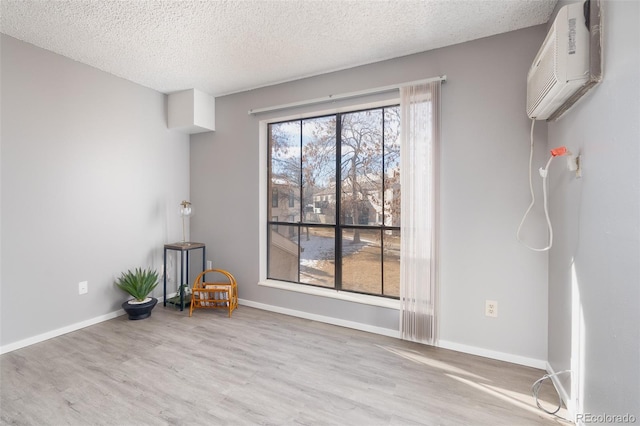 unfurnished room featuring a wall mounted air conditioner, light hardwood / wood-style floors, and a textured ceiling