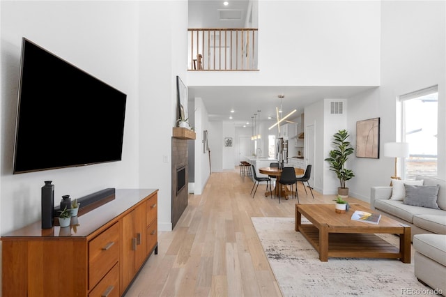 living area featuring visible vents, baseboards, light wood-style flooring, and a towering ceiling