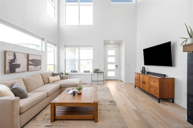 living room featuring light wood-type flooring, baseboards, and a high ceiling