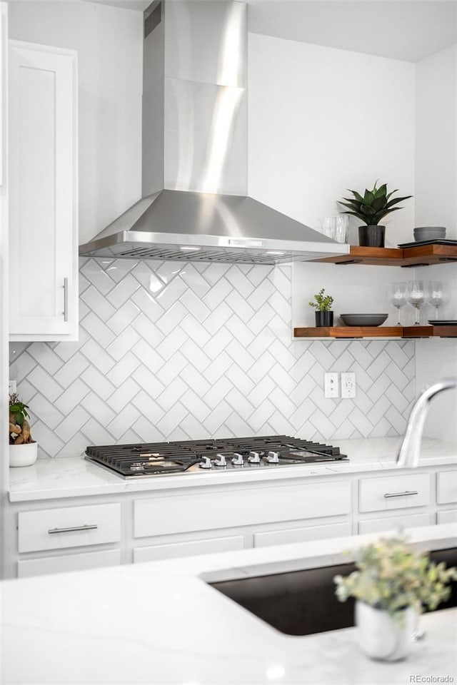 kitchen with stainless steel gas cooktop, white cabinets, tasteful backsplash, and wall chimney exhaust hood