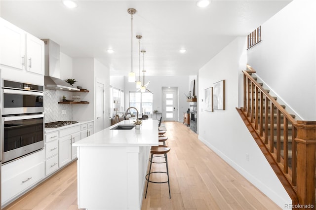 kitchen featuring a breakfast bar, a sink, open shelves, stainless steel appliances, and wall chimney exhaust hood