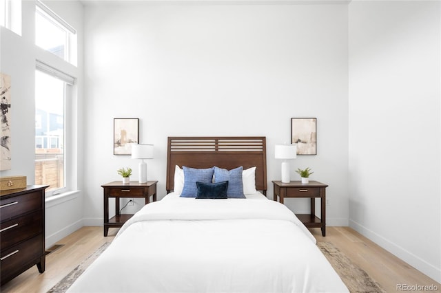 bedroom with a towering ceiling, baseboards, and light wood finished floors