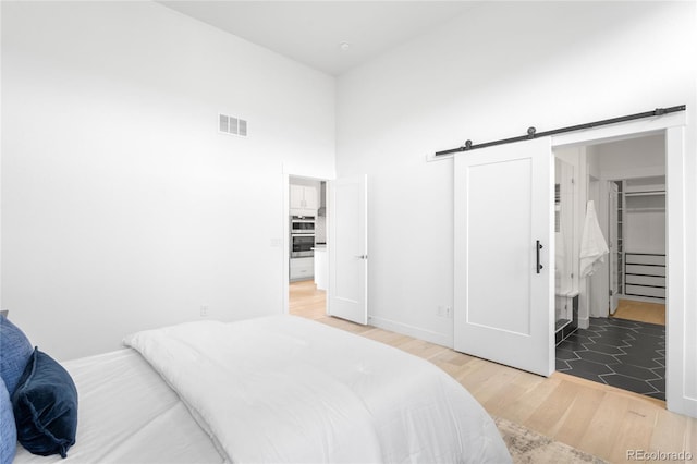 bedroom featuring a barn door, light wood-style flooring, visible vents, and a towering ceiling