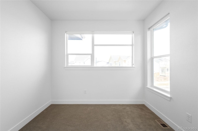 unfurnished room with visible vents, a healthy amount of sunlight, baseboards, and dark colored carpet