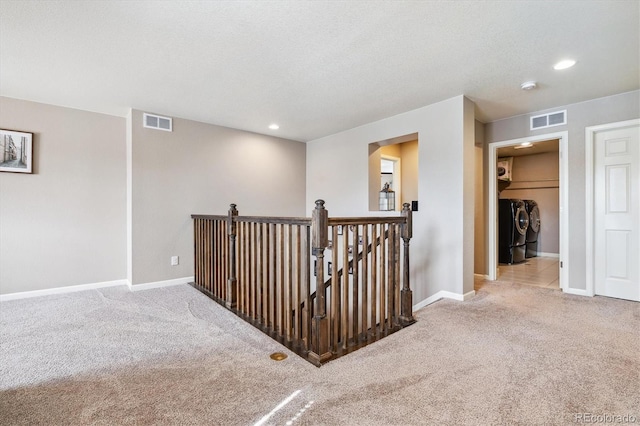 corridor with washing machine and clothes dryer, light carpet, and a textured ceiling