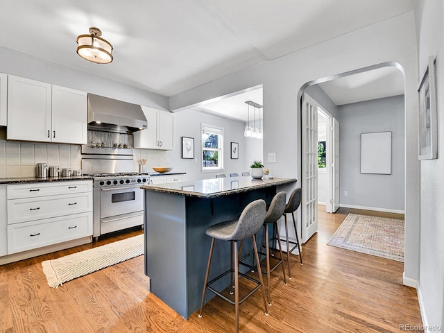 3282 Depew St, Wheat Ridge, CO 80212 - kitchen with high end stainless steel range oven, wall chimney exhaust hood, a breakfast bar area, tasteful backsplash, and white cabinetry