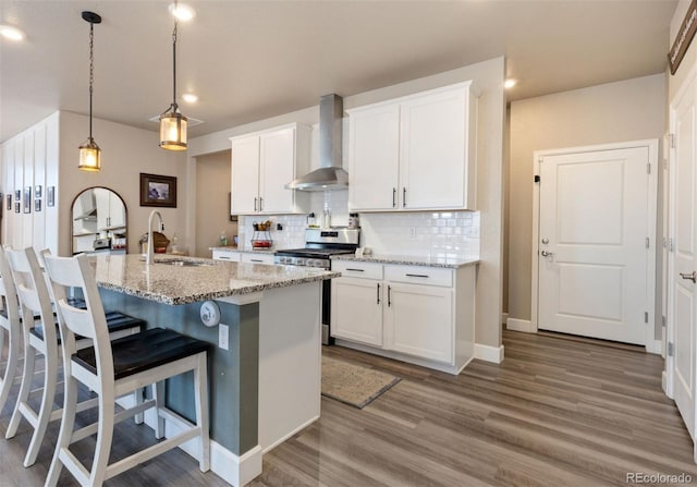 599 Fall River Ct, Brighton, CO 80601 - kitchen featuring wall chimney range hood, stainless steel stove, white cabinets, wood finished floors, and recessed lighting