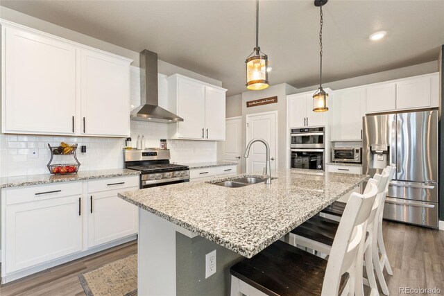 599 Fall River Ct, Brighton, CO 80601 - kitchen featuring appliances with stainless steel finishes, wall chimney range hood, light wood-style floors, decorative backsplash, and white cabinets