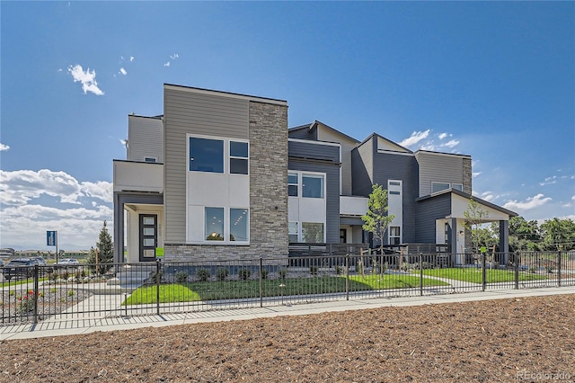 contemporary house with fence private yard, stone siding, and a front yard