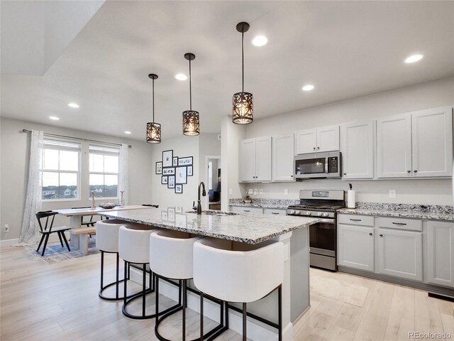 kitchen with stainless steel appliances, a sink, light wood-style floors, recessed lighting, and light stone counters