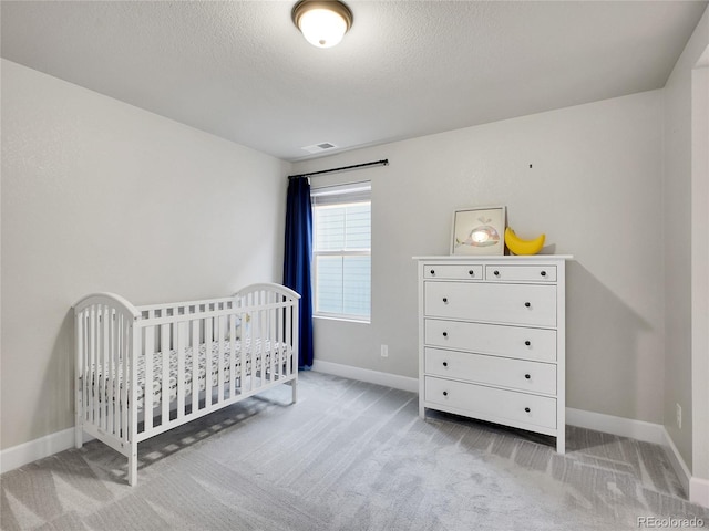 carpeted bedroom with baseboards, a textured ceiling, and a crib