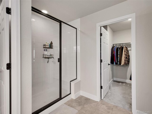 bathroom featuring a shower stall, a spacious closet, tile patterned flooring, and baseboards