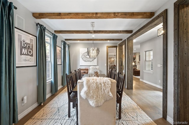 dining room featuring beam ceiling, light wood-type flooring, a wealth of natural light, and a chandelier