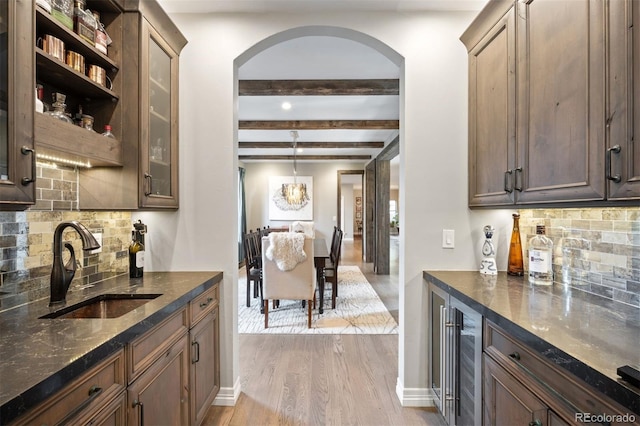 kitchen featuring sink, beverage cooler, beamed ceiling, decorative backsplash, and light wood-type flooring