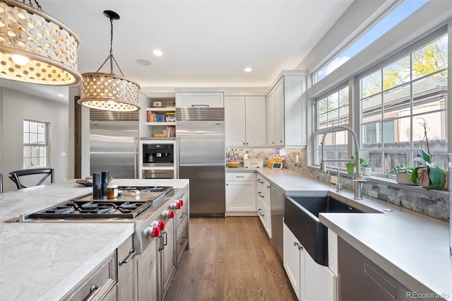 kitchen with pendant lighting, dark wood-type flooring, white cabinets, tasteful backsplash, and stainless steel appliances